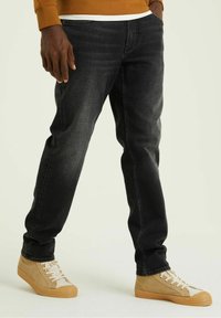 Svarta denimjeans med smal passform, med subtil blekning. I kombination med bruna sneakers som har en strukturerad gummisula och vita snören.