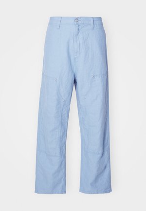 Pantalon en lin bleu clair avec une coupe décontractée, muni de poches plaquées et de détails de coutures visibles. Le tissu a un aspect doux et texturé.