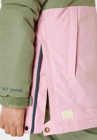 Giacca isolata con parte superiore verde e parte inferiore rosa. Include una tasca con zip, polsini elastici e accenti con marchio. I motivi sono solidi.
