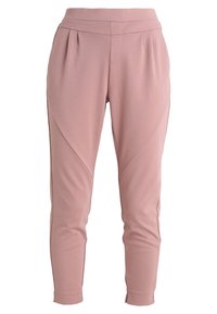 Pantalons rose clair fuselés en tissu lisse, avec des plis sur le devant et des détails de couture sur les côtés, terminés par une taille élastique.