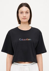 Svart kortärmad t-shirt gjord av mjukt tyg med en flerfärgad "Calvin Klein"-logotyp i en modern stil. Korta ärmar och rund halsringning.
