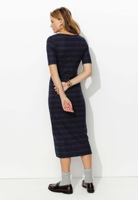 Robe midi à rayures navy avec des manches courtes, design ajusté et col rond. Portée avec des chaussettes grises et des mocassins foncés. Texture lisse.