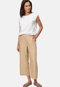 White short-sleeved top with rounded neckline, paired with beige wide-leg trousers featuring side pockets. Tan slip-on shoes with embellishments.