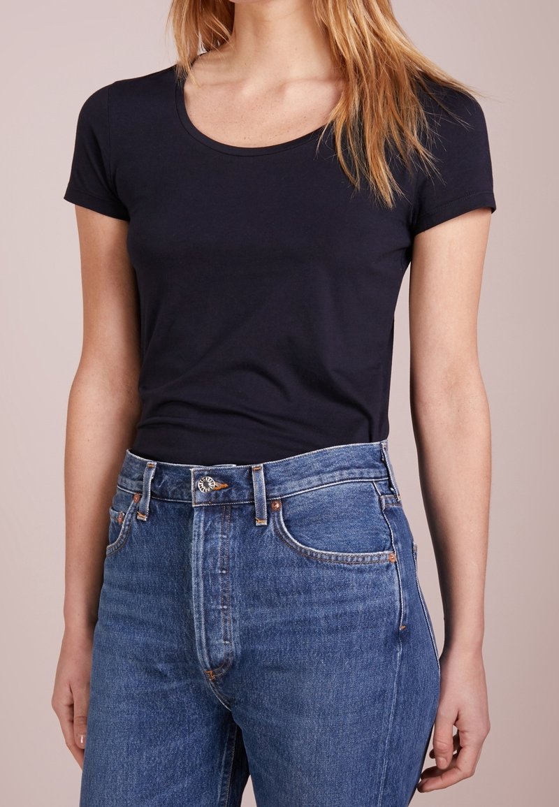 Námořnicky modré tričko s krátkým rukávem vyrobené z měkké tkaniny, spárované s džíny z modrého denimu s vysokým pasem, které mají klasické švy a kovové detaily.