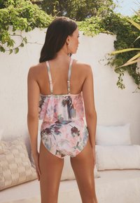 Maillot de bain une pièce fleuri avec un dos à volants, des couleurs rose pastel et vert, des bretelles réglables et une coupe taille mi-haute.