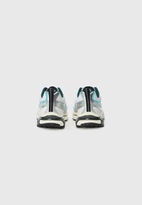 Chaussures de course en argent, noir et turquoise ; tige en mesh et synthétique, semelles rembourrées et semelle extérieure en caoutchouc durable. La vue arrière montre le logo et les accents.
