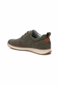 Zapatilla verde con una parte superior texturizada, detalles de cuero marrón y una suela de goma blanca. Presenta un diseño cosido y detalles perforados.
