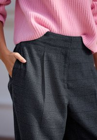 Grijze geruite broek met een gestructureerde stof, voorzien van een hoge taille en zijzakken. Gecombineerd met een geribbelde roze trui.