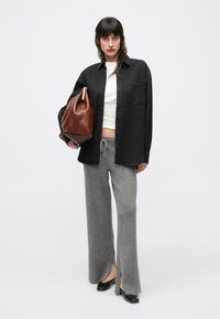 Crna košulja na kopčanje, uska bijela majica, sive široke pletene hlače, crne cipele i smeđa kožna torba s zaobljenim oblikom.