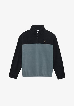 Pull en polaire avec col haut, doté d'une fermeture éclair. Couleurs : bleu marine foncé et teal clair. Logo doré sur la poitrine, texture douce.