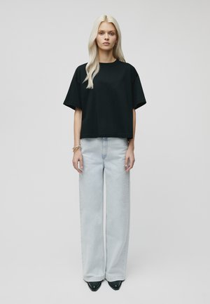 Schwarzes kurzärmliges Crop-Top, kombiniert mit hellblauen weit geschnittenen Jeans. Das Model trägt schwarze spitze Pumps und silberne Armbänder.
