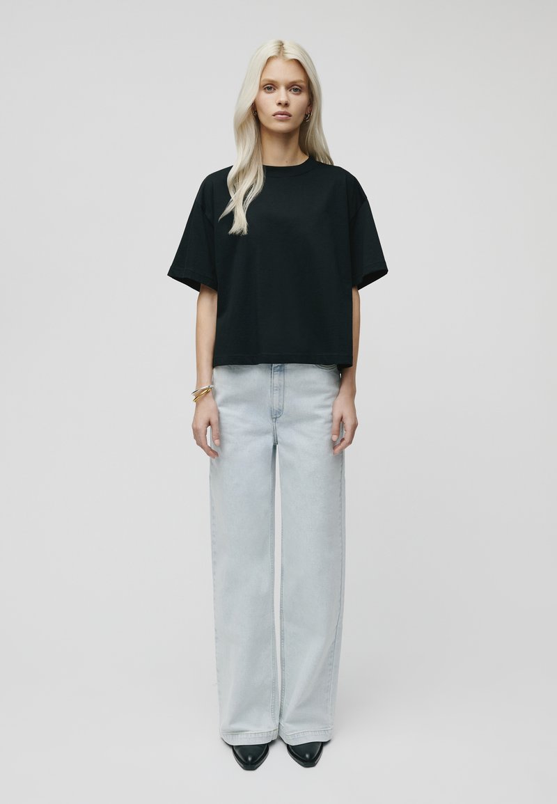 Black cropped t-shirt with short sleeves, paired with light blue wide-leg jeans. Model wears black pointed-toe heels and silver bracelets.