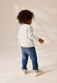 Maglione grigio chiaro con polsini a costine, jeans di denim blu con orli risvoltati e sneakers beige. Tessuto morbido e vestibilità casual, visto da dietro.