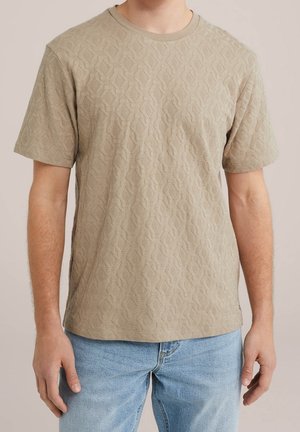 Korte mouwen, lichtbruin overhemd met een gestructureerd geometrisch patroon, ronde halslijn en een relaxte pasvorm. Gecombineerd met een blauwe spijkerbroek.