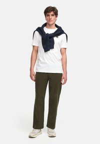 Camisa blanca de cuello redondo, pantalones verde oliva de pierna recta y un sudadera azul marino atada alrededor de los hombros. Footwear casual.