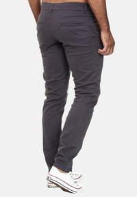 Graue Baumwollhosen mit schlanker Passform, ausgestattet mit Gesäßtaschen und dezenten Stickdetails. Kombiniert mit weißen Sneakers.