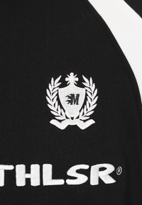 Fekete szövet, amelyen fehér hímzett logó látható, koronás pajzs és babérlevelek motívummal, a „ATHLSR” fehér felirattal kísérve.