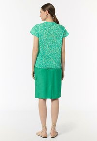Green top with a leopard print in light cream tones, paired with a solid green knee-length skirt featuring a side pocket.