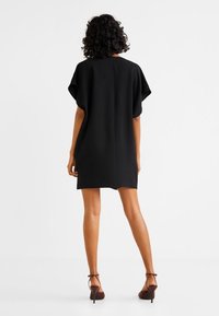 Schwarzes kurzes Kleid mit lockerer Passform, kurzen Ärmeln und geradem Saum. Glattes Material mit einem dezenten Rückennahtdetail.