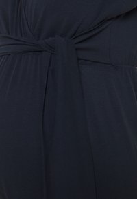 Navy blauw jurkje van een zachte, rekbare stof met een strikdetails in de taille en een subtiele gathering bij de buste voor een ontspannen pasvorm.