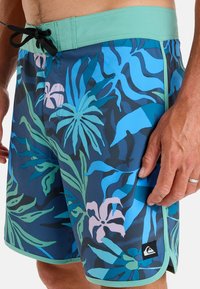 Badbyxor med ett blått och grönt tropiskt bladmönster, lätt material, elastisk midja med mintgrönt kantband och sidoficka.