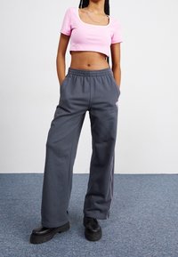 Ljust rosa kort topp med fyrkantig halsringning, kombinerad med mörkgrå byxor med vida ben som har en rosa sidosträng och elastisk midja.