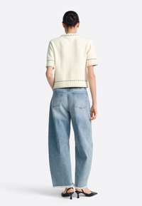 Suéter crema de manga corta con detalles de costura en negro, combinado con jeans de pierna ancha azul claro con dobladillos deshilachados y tacones negros sin cierre.