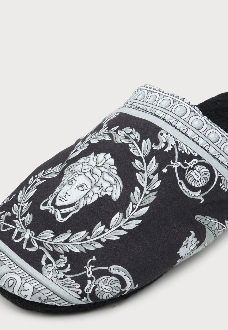 Pantofole nere slip-on con un intricato design bianco classico della testa di Medusa e motivi decorativi a corona d'alloro e volute.
