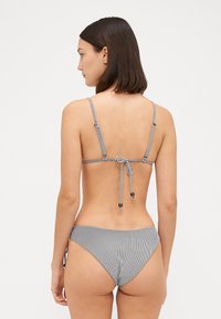 Bikini a righe bianche e nere con chiusura a laccio e spalline regolabili, con slip coordinati che riprendono il design a righe.