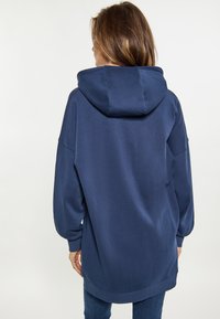 Sudadera oversized azul marino con un acabado texturizado, que presenta una gran capucha y puños acanalados, vista desde atrás. Diseño minimalista y casual.