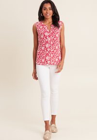 Top rosso floreale senza maniche con scollo a V, abbinato a pantaloni skinny bianchi e scarpe slip-on beige.