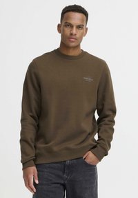 Sudadera marrón hecha de un tejido suave, con cuello redondo y puños acanalados. Texto impreso en el pecho que añade un detalle minimalista.