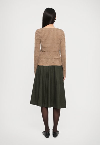 Beige ribbed sweater with long sleeves paired with a dark green flared skirt. Black shoes with silver accents. Back view of the outfit.