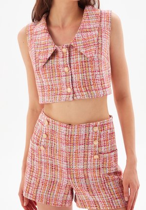 Femme portant un crop top sans manches à carreaux roses et blancs avec un grand col et un short taille haute assorti avec des boutons et des poches.