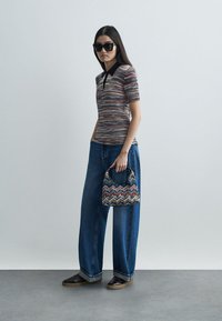 Pletiva majica polo s višenamjenskim uzorkom, uparena s širokim plavim trapericama. Manja, torbica s uzorkom i tamne sunčane naočale upotpunjuju izgled.