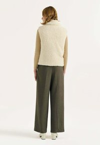 Chaleco sin mangas blanco y esponjoso con un cuello alto, combinado con pantalones grises sueltos y zapatos de tacón cuadrado blancos. Tela simple y texturizada.