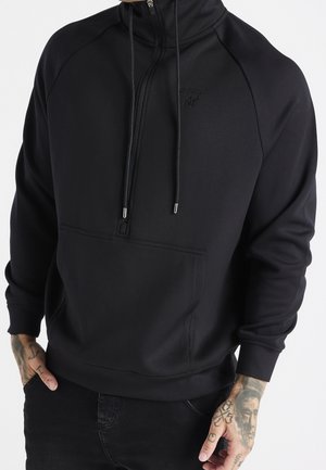 Sudadera con capucha negra, con cuello alto, media cremallera, bolsillo delantero y cordones. Presenta una textura suave y un detalle de logotipo sutil.