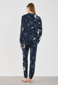 Ensemble de pyjama bleu marine avec des motifs célestes, incluant des soleils, des lunes et des étoiles ; fabriqué en tissu doux, avec des manches longues et un pantalon ajusté.