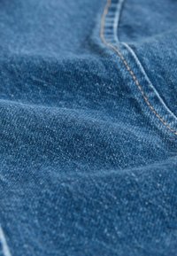 Sötétkék farmeranyag texturált szövettel és finom kifakulással. Látható varrások kontrasztos barna cérnával.