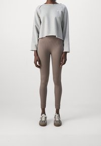 Sweatshirt gris coupé avec des bords effilochés, assorti à un legging côtelé marron clair. Les chaussures présentent un motif à carreaux et un design à lacets.