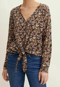 Blusa nera con stampa floreale, scollatura a V, chiusura frontale con bottoni e dettaglio con fiocco davanti. Maniche lunghe con polsini a bottoni. Tessuto leggero.