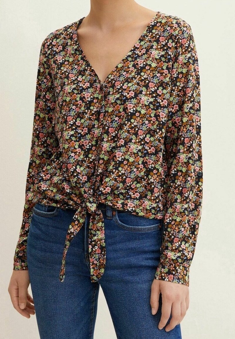 Blusa nera con stampa floreale, scollatura a V, chiusura frontale con bottoni e dettaglio con fiocco davanti. Maniche lunghe con polsini a bottoni. Tessuto leggero.