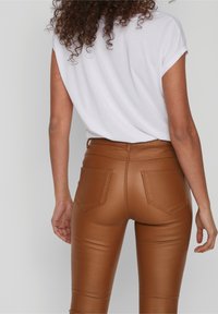Hnědé kalhoty z umělé kůže s přiléhavým střihem, vysokým pasem a dvěma zadními kapsami. Kombinovány s jednoduchým bílým tričkem s krátkým rukávem.