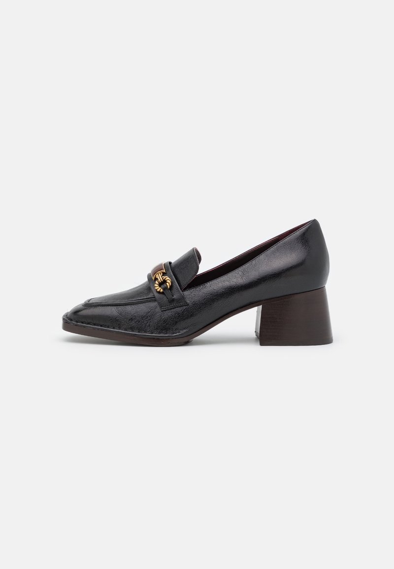 Mocassin en cuir noir à talon moyen, bout pointu et détail chaîne dorée sur le cou-de-pied, présenté sur un fond blanc.