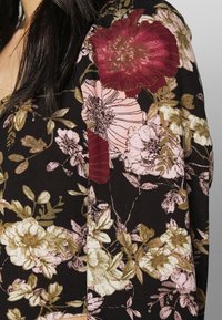 Tessuto nero con grandi motivi floreali in marrone, rosa e oro. Texture morbida con una leggera lucentezza, che mette in evidenza dettagliate decorazioni fogliari.