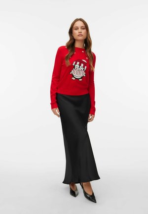 Un pull en tricot rouge avec un motif de pingouin et des flocons de neige, associé à une longue jupe en satin noire et des escarpins noirs à bout pointu.