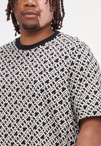 T-skjorte med kort erm i svart og hvitt med et geometrisk mønster. Har svart krage og en liten logo-detalj. Laget av bomull.
