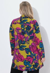 Košile s dlouhým rukávem s živým květinovým vzorem v růžové a modré na hořčicově žlutém pozadí; volný střih, detail s plisem na zadní straně a bočními rozparky.