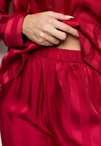 Rotes Satin-Loungewear-Set mit gestreiftem Design, lockerer Passform des Oberteils mit Knopfverschluss und Hose mit elastischem Bund. Weiche, glatte Textur.