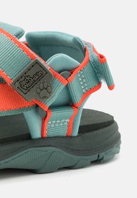 Teal outdoor sandal with orange accents, featuring adjustable straps, textured footbed, and rugged rubber sole, branded with Jack Wolfskin logo.
